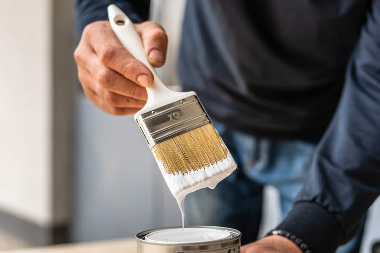 Paint Brush Application Painter's hand holding angled brush dripping white paint over open can indoors