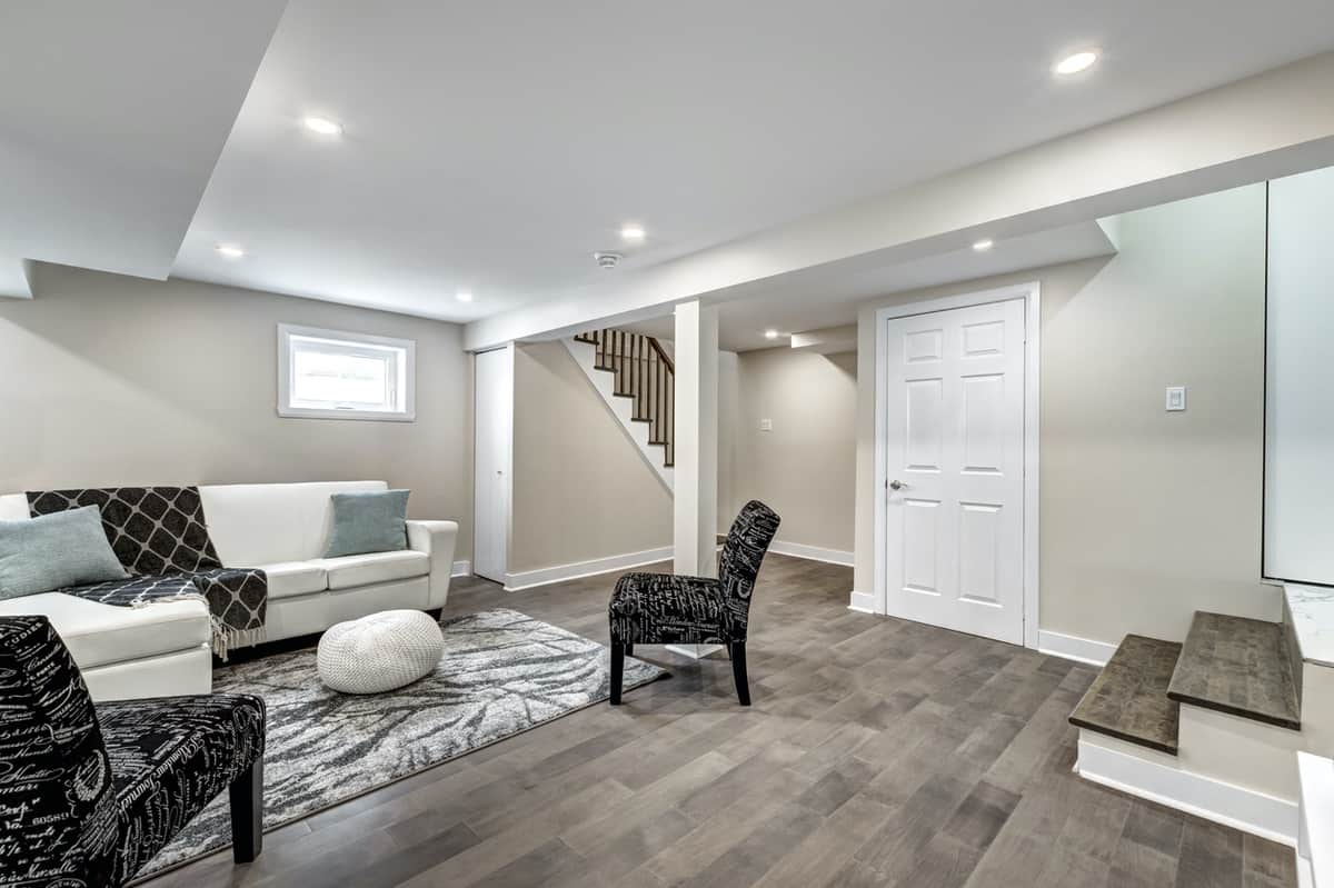 Beige Basement Interior Painting Beige painted basement interior with white trim, recessed ceiling lights, staircase, and dark wood-tone flooring in Saint