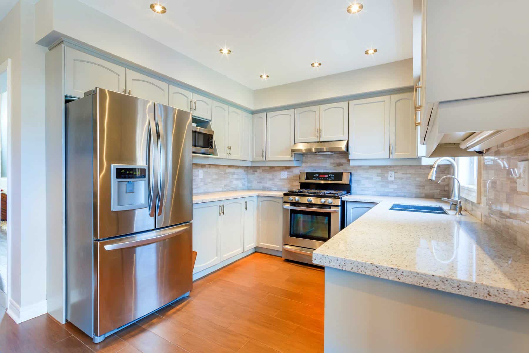 Bright white painted kitchen cabinets with stainless steel appliances, granite countertop, and wood flooring