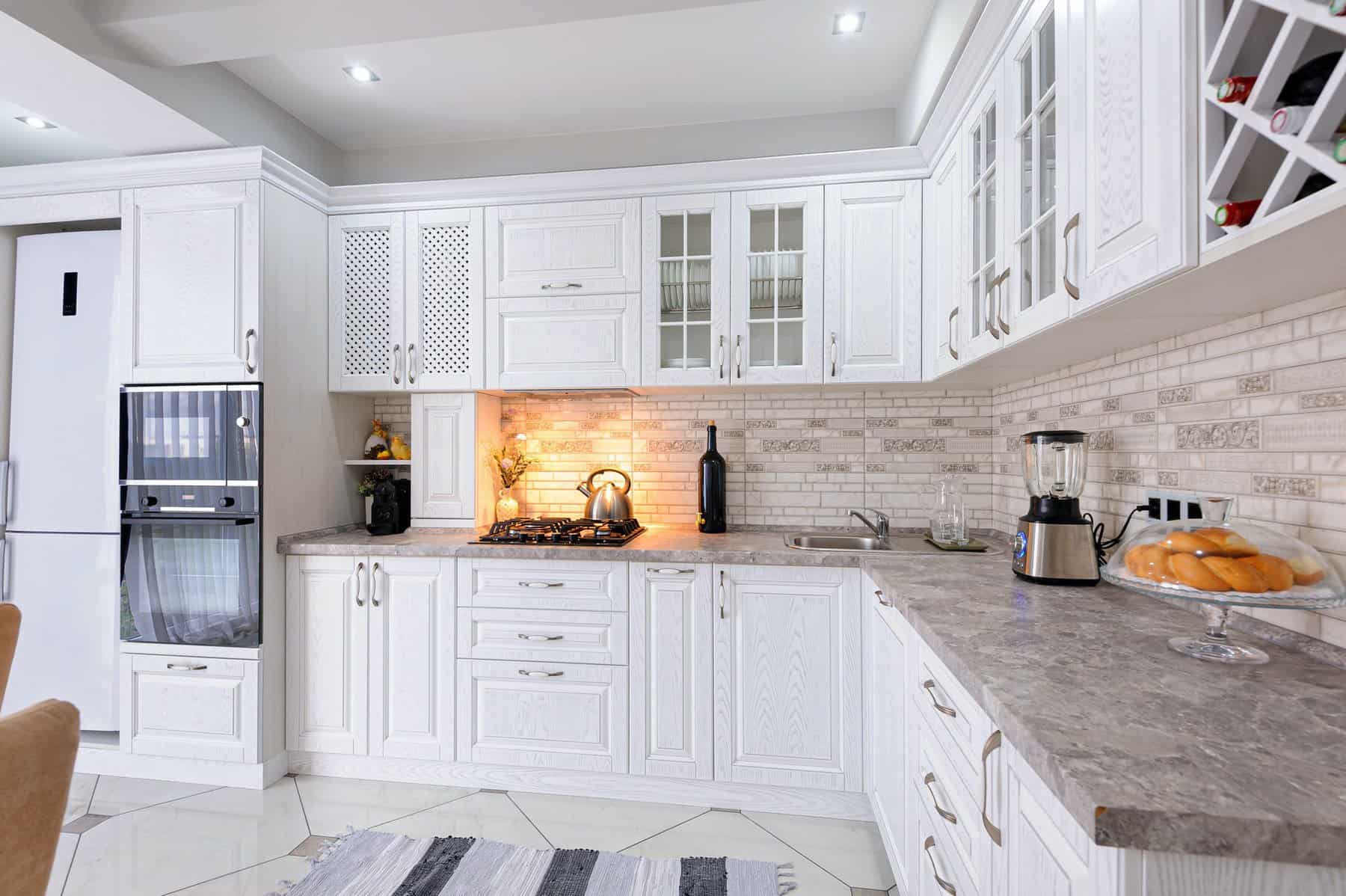 Bright white painted kitchen cabinets with glass-front doors, granite countertop, subway tile backsplash, and stainless