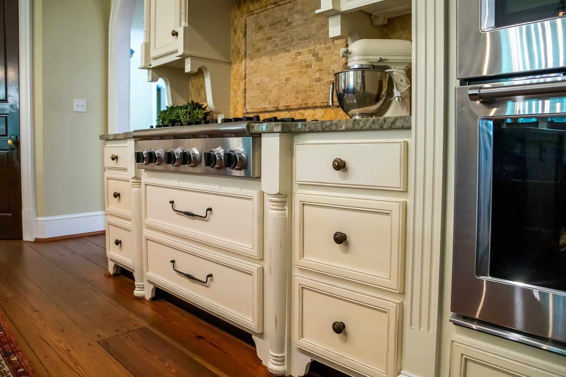 Cream-painted kitchen island and cabinetry with black hardware, granite countertop, and stainless steel appliances