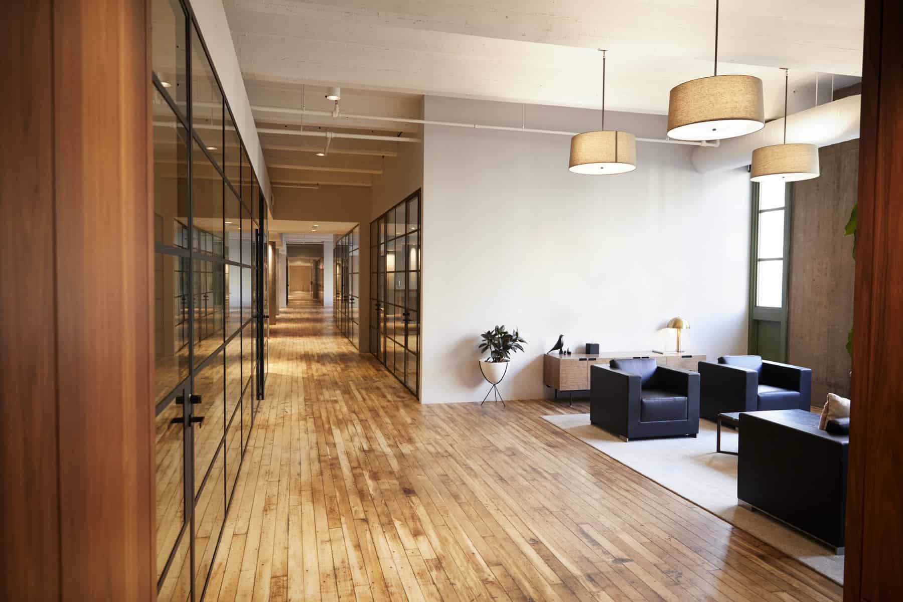 Commercial Interior Painters Bright white painted commercial interior with wood flooring, glass-partitioned offices, and pendant lighting