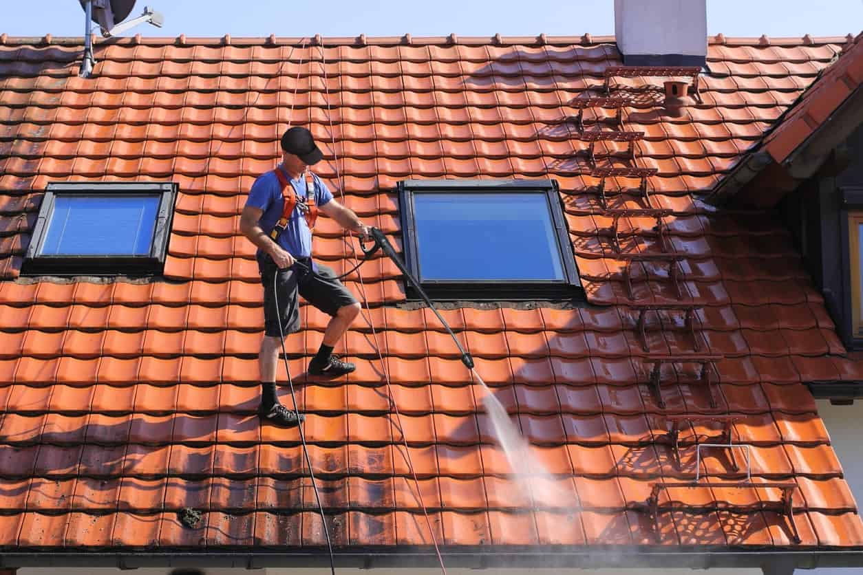 Roof Pressure Washing Service Worker pressure washing clay tile roof with high-pressure spray on residential home with skylights