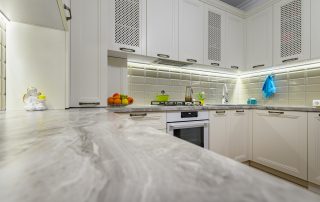 Cream-painted kitchen cabinetry with perforated upper doors, marble countertop, beige subway tile backsplash, and stainless cabinet and countertop color combinations