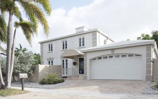 Light gray and white two-story residential home with white garage door, covered entry porch, and paver driveway