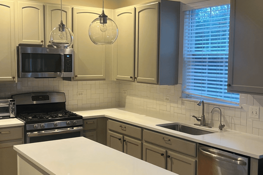 Cream upper and gray lower kitchen cabinets with white subway tile backsplash, stainless steel appliances, and pendant