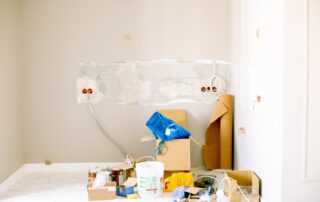 Cream-colored interior wall with protective plastic sheeting, painter's supplies, and cardboard boxes during residential