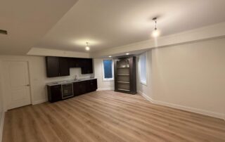 Cream-painted basement interior with white trim, dark cabinetry, wood-look flooring, and recessed ceiling lights.