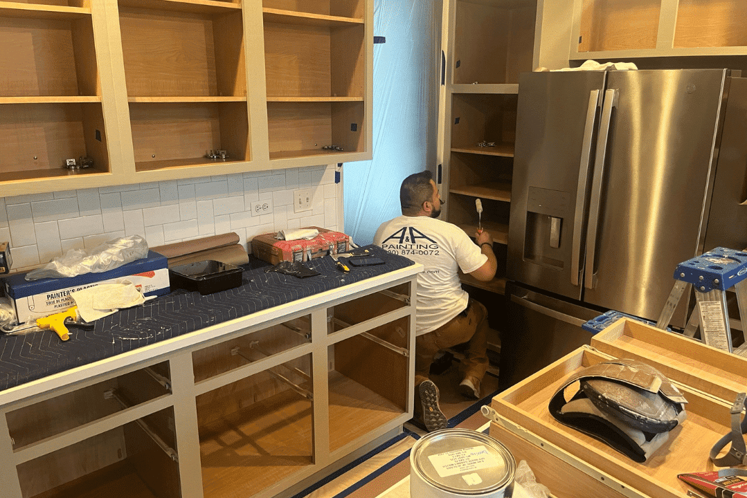 Painter working on natural wood kitchen cabinets during interior residential refinishing with white subway tile backsplash