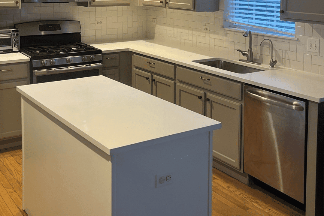 Cream-painted upper cabinets and blue island with white countertops in residential kitchen during interior painting.