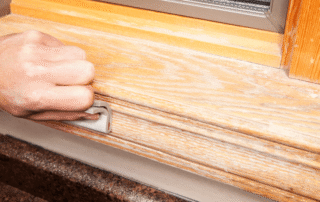 Hand inspecting natural wood window sill with visible grain texture and stain finish during interior residential painting