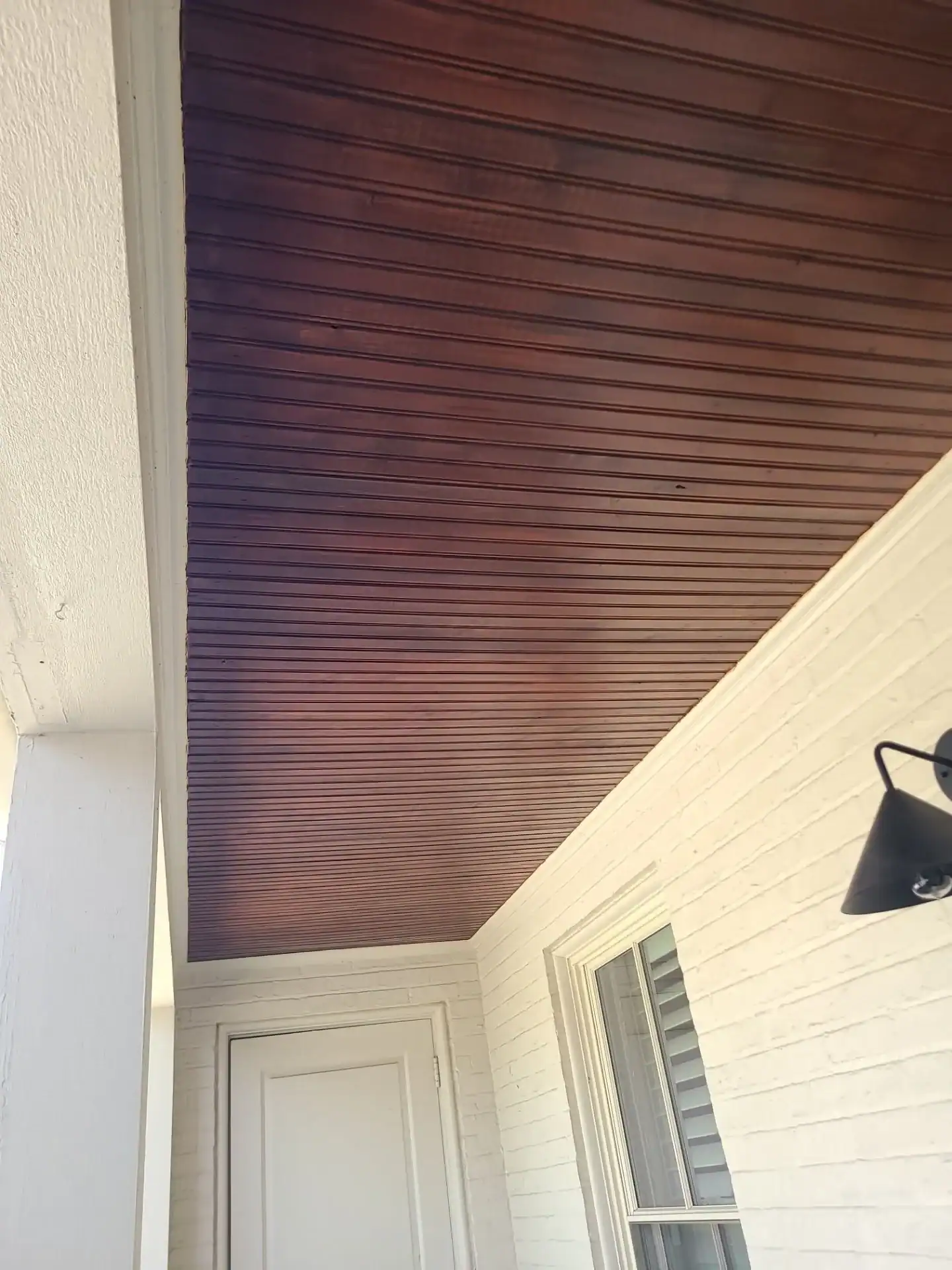 Dark Brown Porch Ceiling Paint Dark brown painted porch ceiling with horizontal wood planking above cream-painted horizontal vinyl siding residential