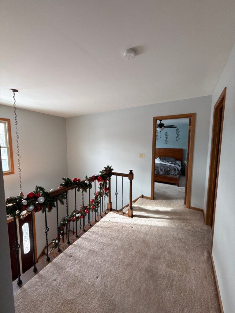 White Painted Upstairs Hallway White-painted residential upstairs hallway with beige carpeting, wood-trimmed doorways, and stair railing decorated with