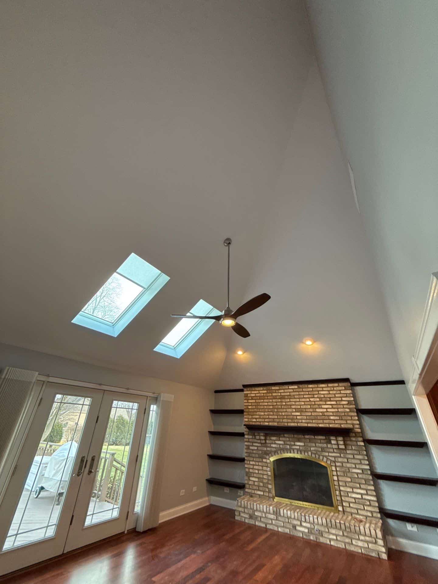 Taupe Vaulted Ceiling Interior Taupe-painted vaulted ceiling with skylights, ceiling fan, recessed lighting, and brick fireplace in residential interior.