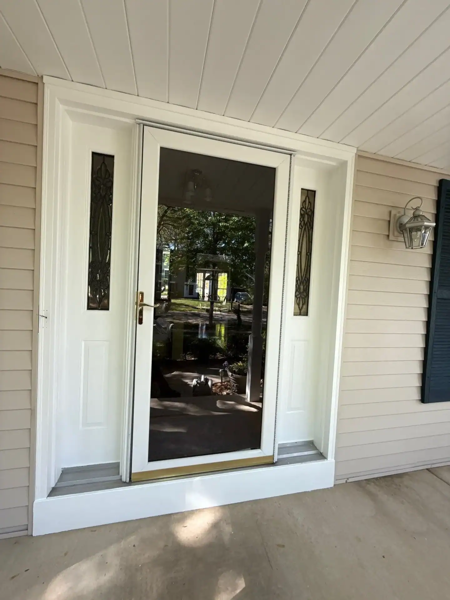 Cream-painted residential porch surround with white-trimmed black screen door, sidelights, and beige vinyl siding.