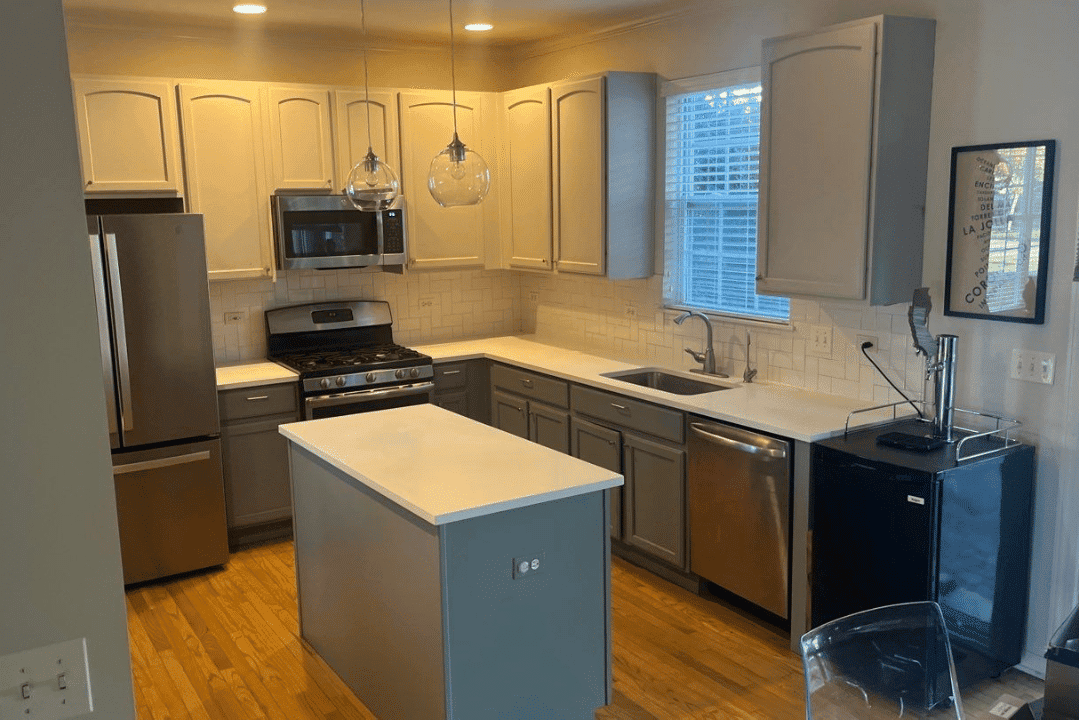 Cream and gray painted kitchen cabinets with white quartz countertops, stainless steel appliances, and wood flooring.