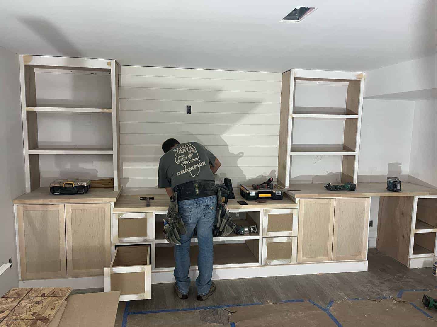 Residential Garage Cabinet Installation Worker installing light wood-tone cabinetry with white shiplap backsplash and open shelving in residential garage
