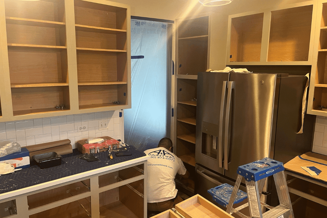 Cream-painted kitchen cabinets mid-refinishing with white subway tile backsplash, stainless steel appliances, and blue