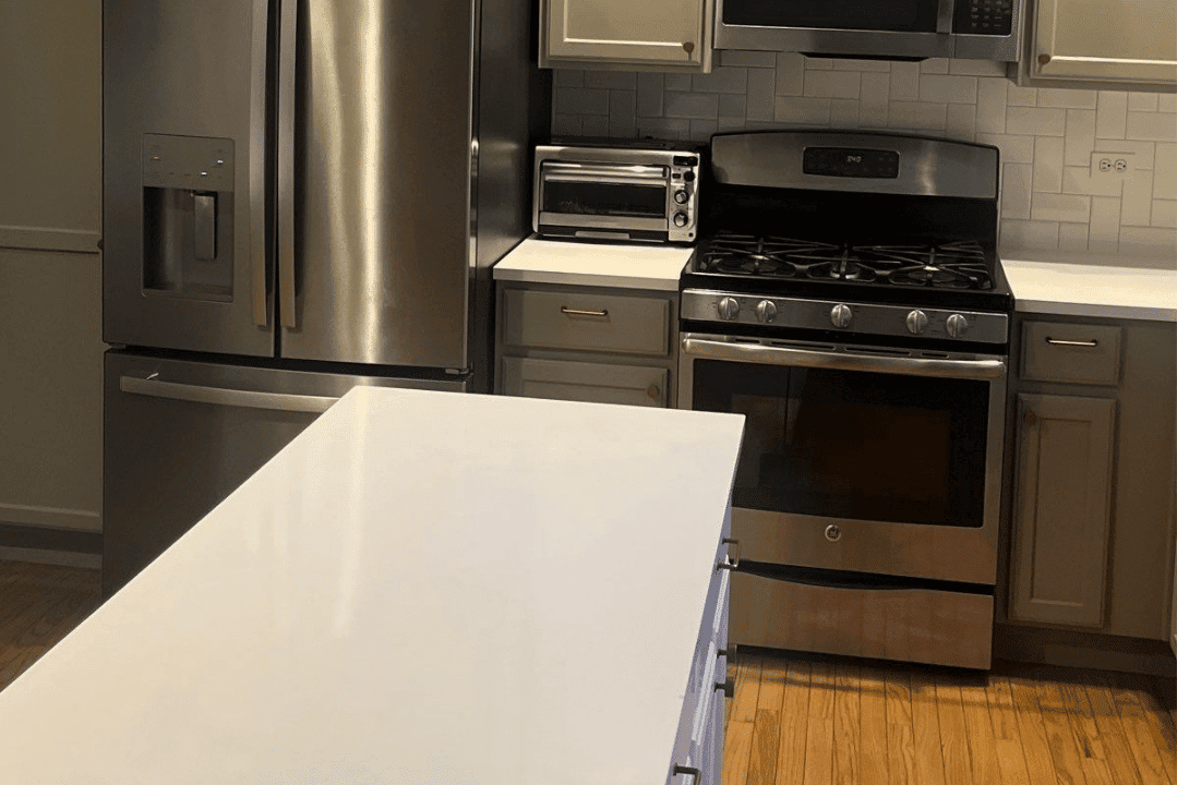 Cream-painted kitchen cabinets with white quartz countertop, stainless steel gas range, and wood flooring in residential