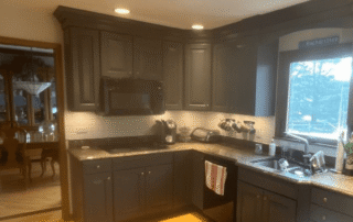 Charcoal-painted kitchen cabinetry with raised-panel doors, granite countertops, and cream backsplash tile.
