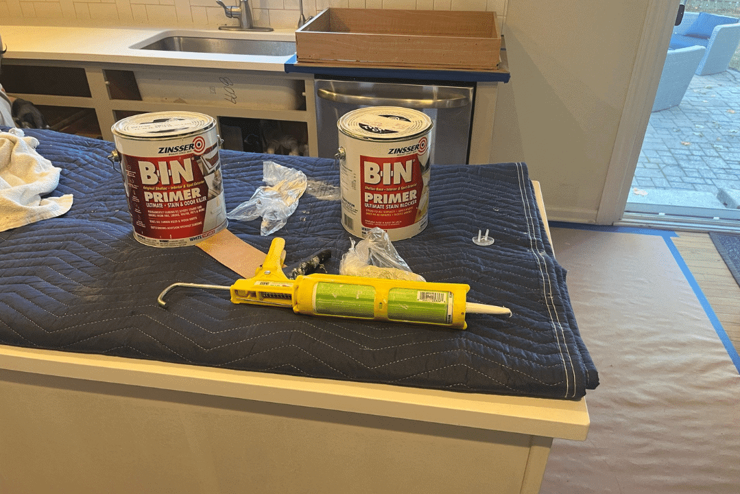 BIN primer cans and caulking gun on blue drop cloth covering kitchen countertop during interior residential cabinet