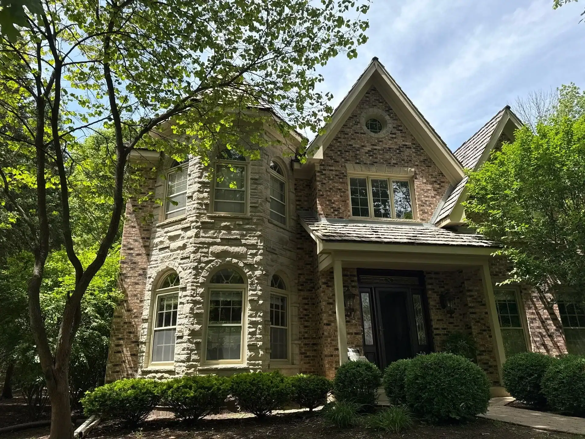 Brick Residential Home Exterior Red and tan brick two-story residential home with stone accents, metal roof, green-trimmed windows, and black entry door in