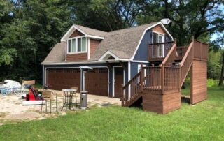 Dark blue two-story residential home with cream trim, brick foundation, attached garage, and front deck in Saint Charles, IL