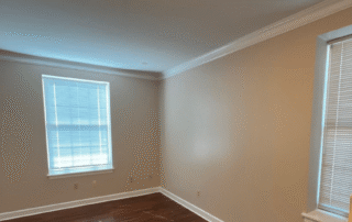 Tan-painted residential bedroom with white crown molding, white trim, dark wood flooring, and two windows with blinds
