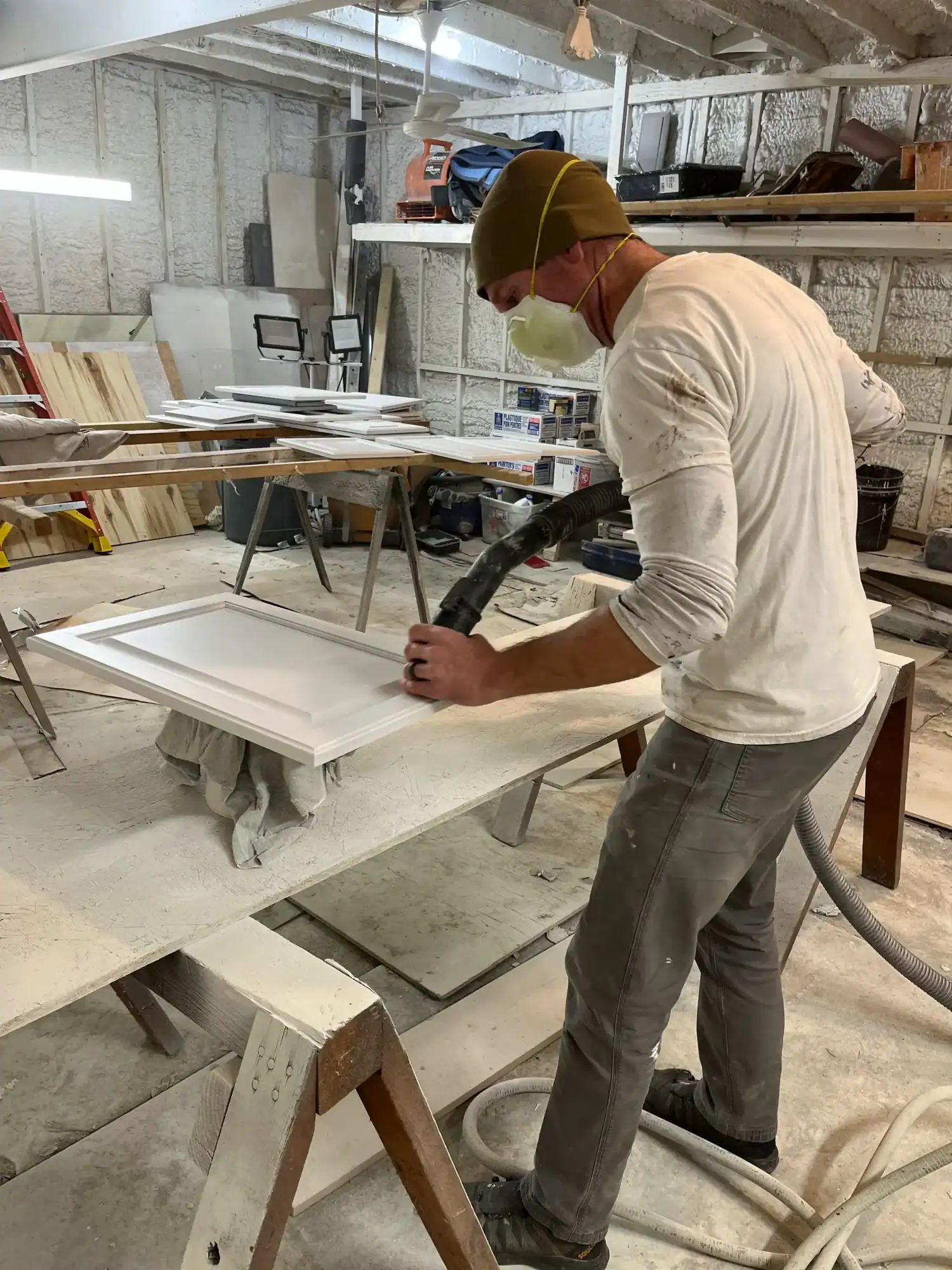 Cabinet Door Spray Finishing Painter in olive cap and white shirt spray-finishing white cabinet door on work table in industrial workshop.