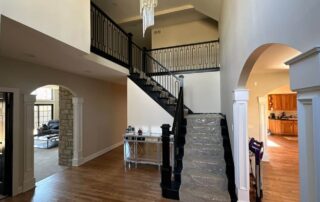 Cream and white painted residential stairway with black metal railing, arched doorways, and wood flooring