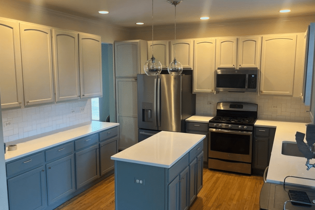 Two-Tone Kitchen Cabinet Painting Two-tone kitchen with cream upper cabinets, blue lower cabinets, white countertops, stainless steel appliances, and pendant