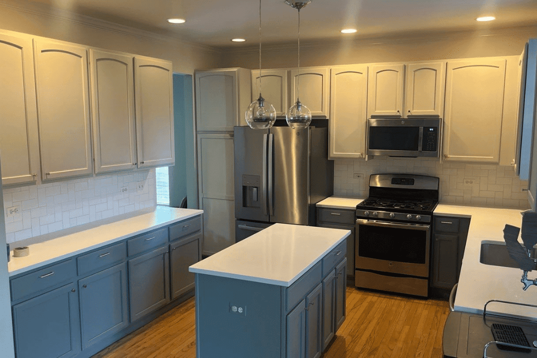 Two-Tone Kitchen Cabinet Painting Two-tone kitchen with cream upper cabinets, blue lower cabinets, white countertops, stainless steel appliances, and pendant