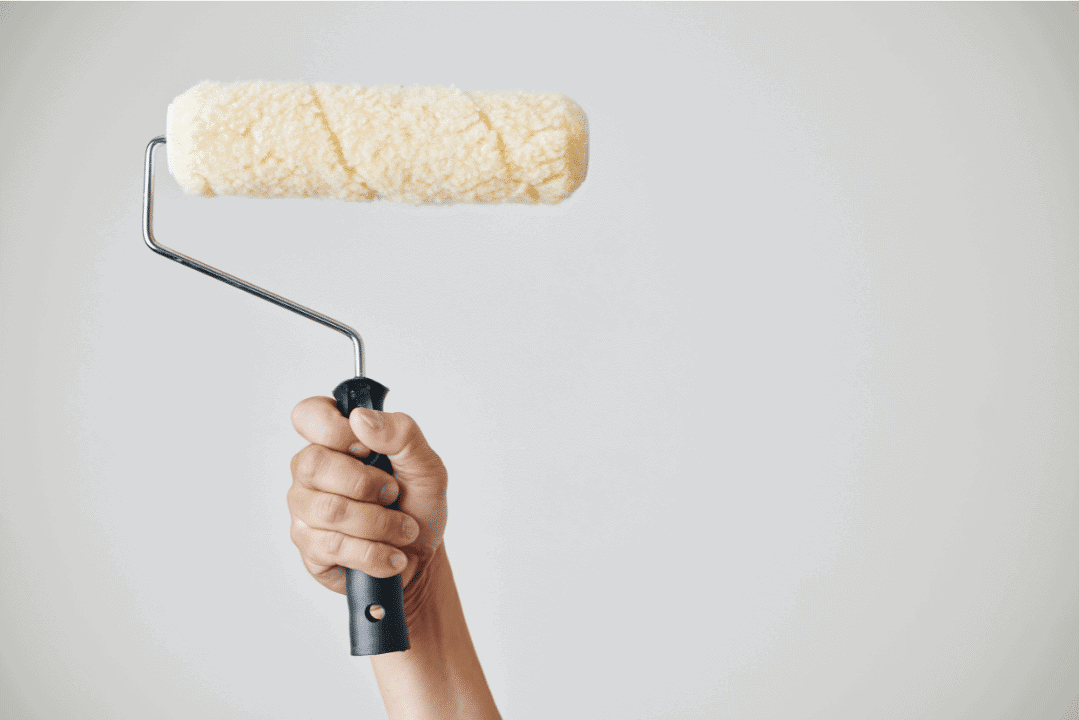 Cream Paint Roller Application Hand holding cream-colored paint roller with black handle raised against neutral background.