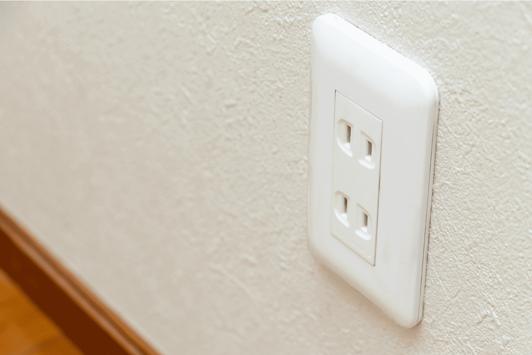 White Interior Electrical Outlet White double electrical outlet mounted on cream-painted interior residential wall with textured finish.
