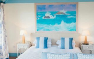 Cream-painted residential bedroom with turquoise exposed beams, white trim, and coastal ocean artwork above bed.