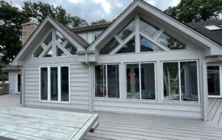 White-painted residential home exterior with gray roof, white-trimmed windows, and composite deck.