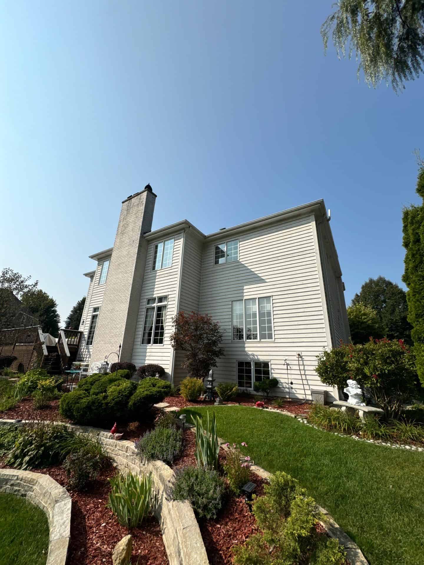 Cream Residential Home Exterior Painting Cream-painted two-story residential home with brick chimney, white-trimmed windows, horizontal vinyl siding, and landscaped