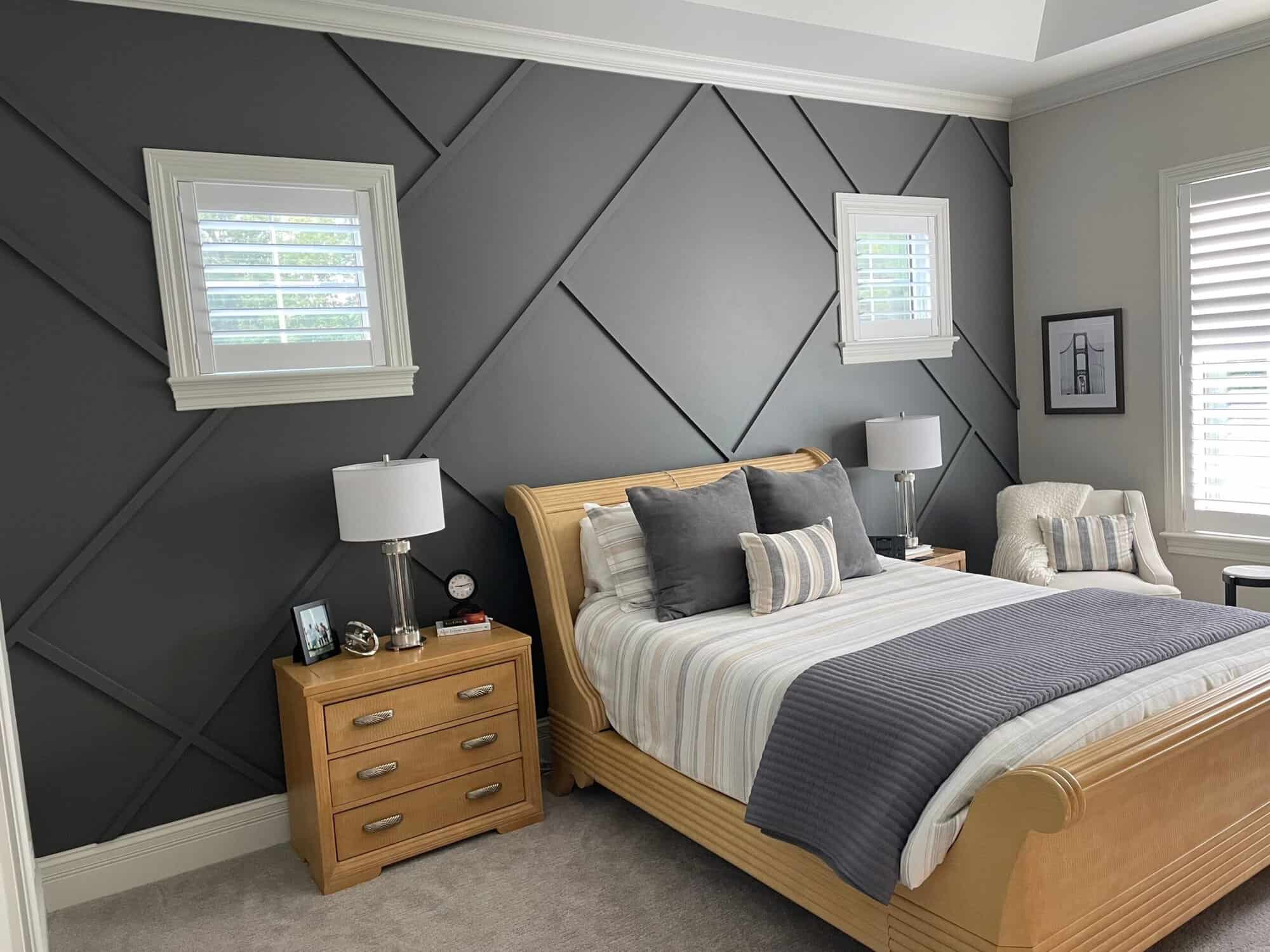 Charcoal Gray Geometric Accent Wall Bedroom Charcoal-painted residential bedroom with geometric diamond pattern wall, white trim, wood bed frame, and white-shuttered