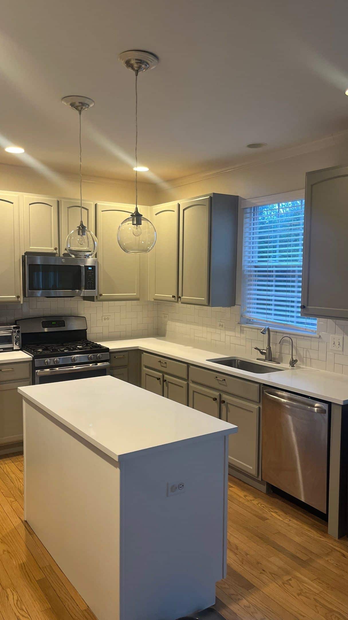Cream Kitchen Cabinetry Renovation Cream-painted residential kitchen with white subway tile backsplash, white quartz island, stainless steel appliances, and