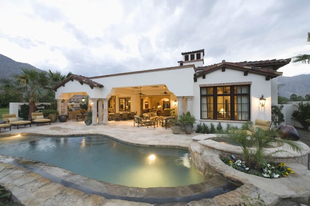 White Stucco Home Exterior Painting White stucco exterior residential home with dark wood beams, arched covered patio, and illuminated interior spaces.