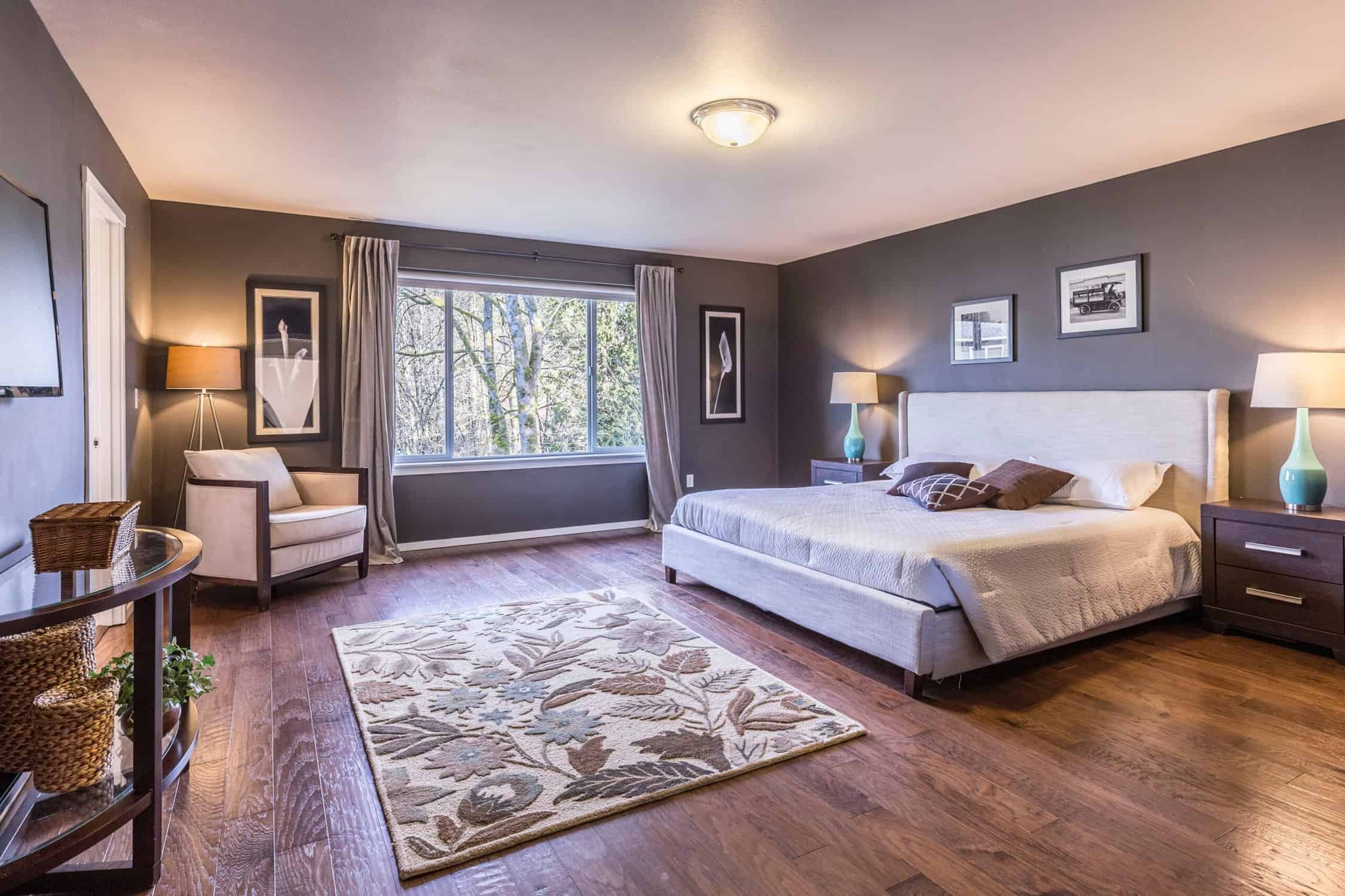 Gray Painted Master Bedroom Gray-painted residential master bedroom with white upholstered bed, warm wood flooring, area rug, and large windows.