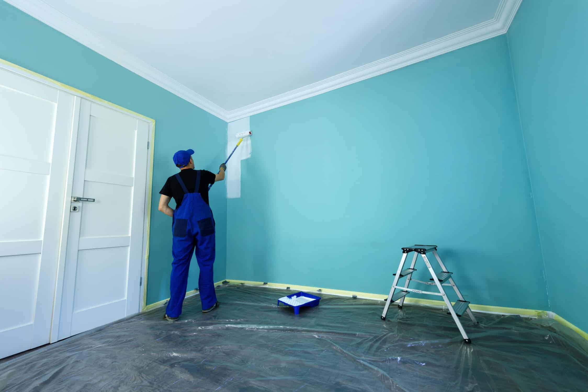 Turquoise Interior Room Painting Painter in blue uniform applying turquoise paint to residential interior wall with white trim and protected flooring.