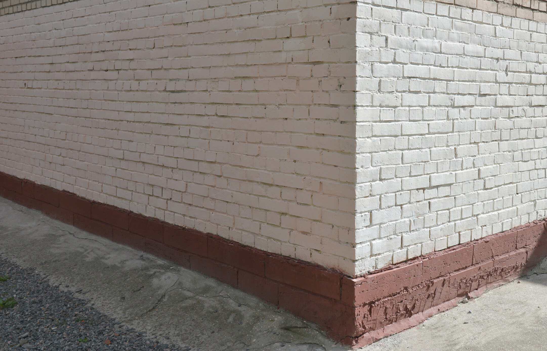 Cream Brick Exterior with Red Base Cream-painted brick exterior wall with red brick base trim on residential building corner.