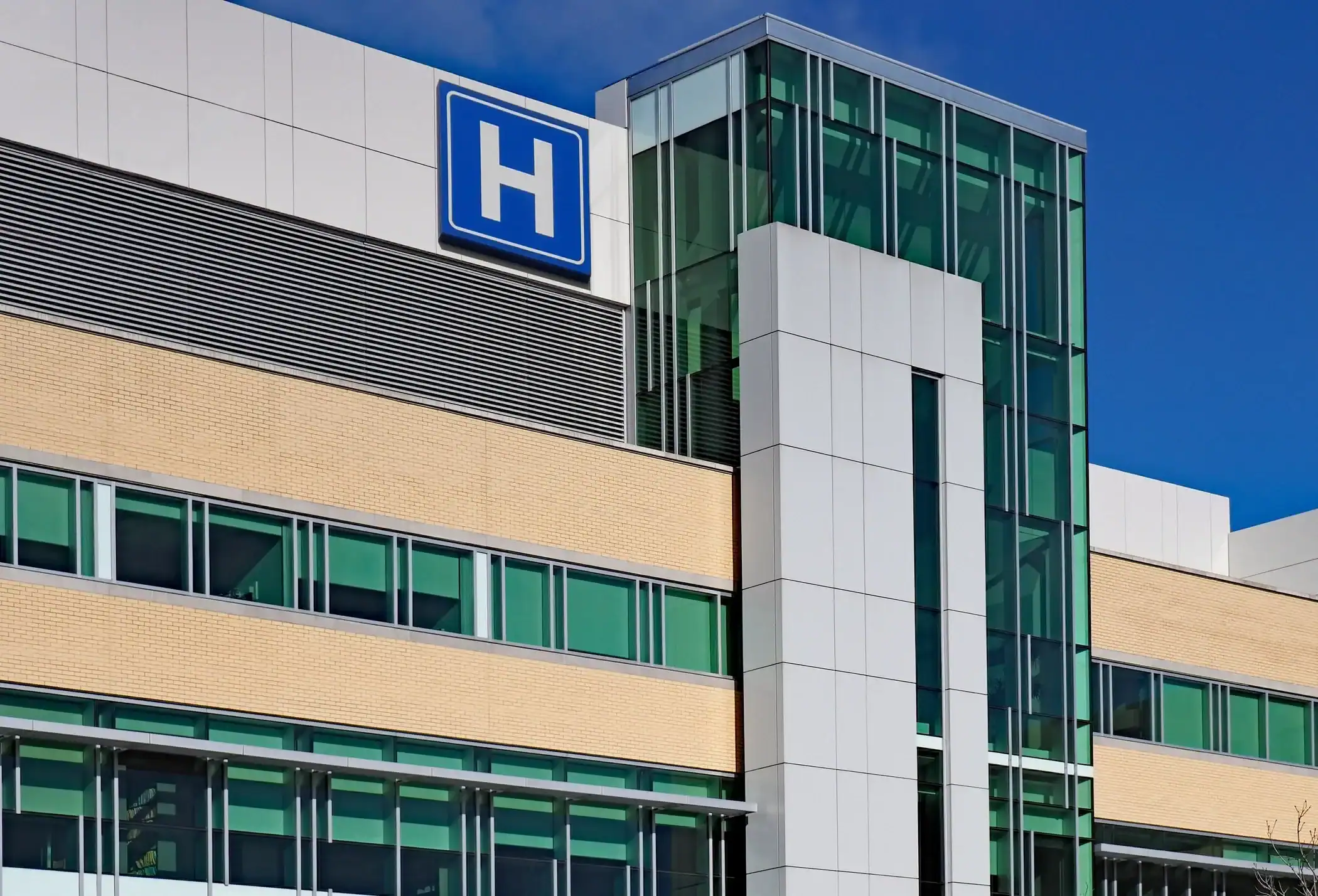 Hospital Building Exterior Painting White-painted commercial hospital building with cream brick band, green-framed windows, and blue hospital signage.
