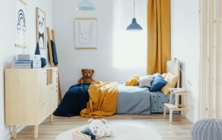 White-painted residential child's bedroom with light wood flooring, natural wood furniture, blue and yellow bedding, and