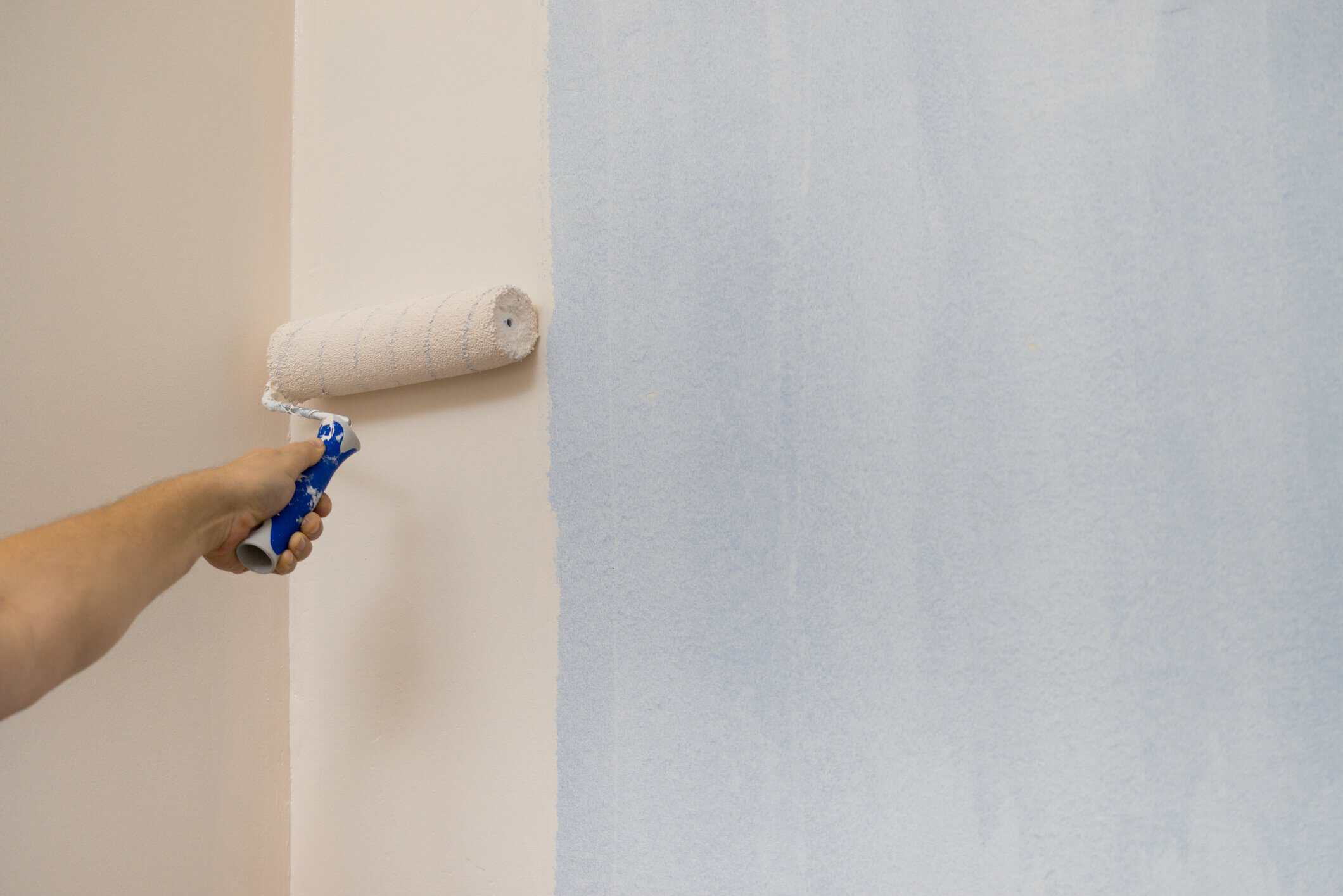 Interior Residential Wall Painting Painter with blue glove applying cream paint to interior drywall with paint roller.