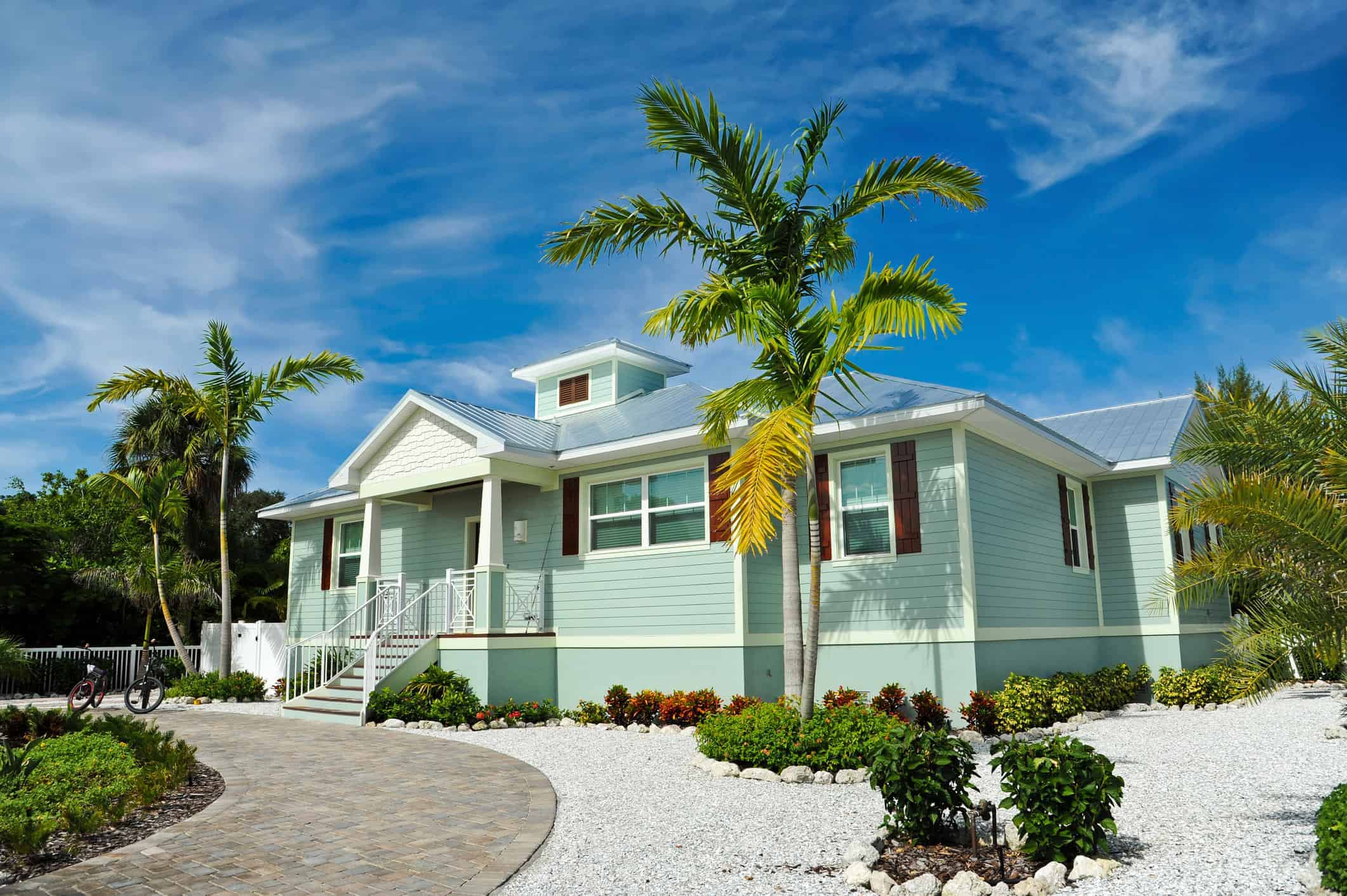 Light Blue Coastal Home Exterior Light blue residential home exterior with white trim, metal roof, covered porch, and brick paver driveway in Saint Charles
