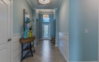 Light blue-painted residential hallway with white wainscoting, white-trimmed doors, gray tile flooring, and ceiling fixture.