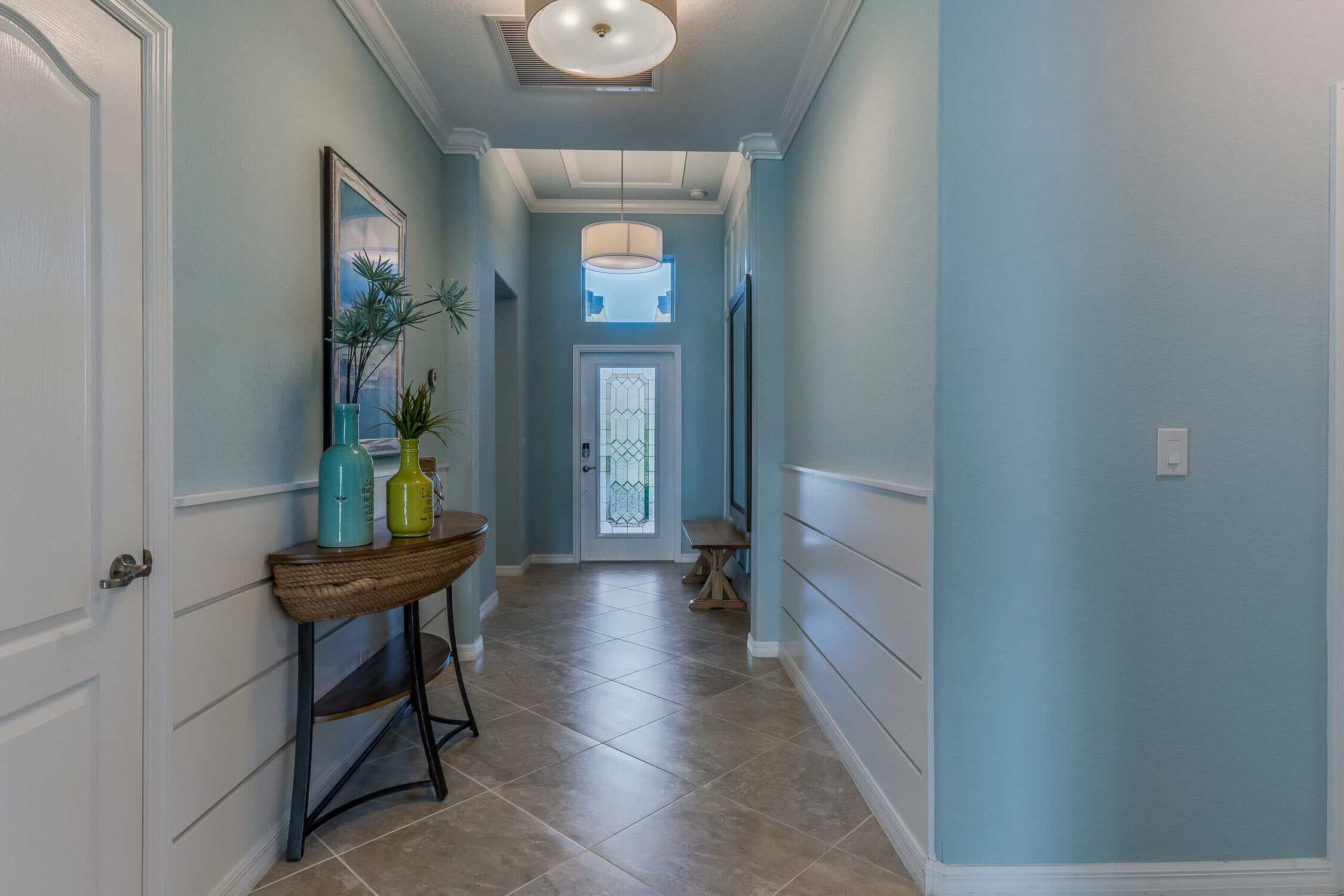 Light Blue Hallway Interior Painting Light blue-painted residential hallway with white wainscoting, white-trimmed doors, gray tile flooring, and ceiling fixture.