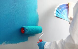 Turquoise paint being rolled onto white drywall with color swatch fan nearby during interior residential painting.